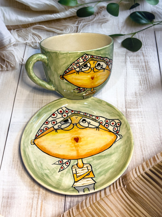 Green ceramic mug and saucer hand-painted with girl wearing glasses and polka-dot scarf, displayed on wooden textured background.